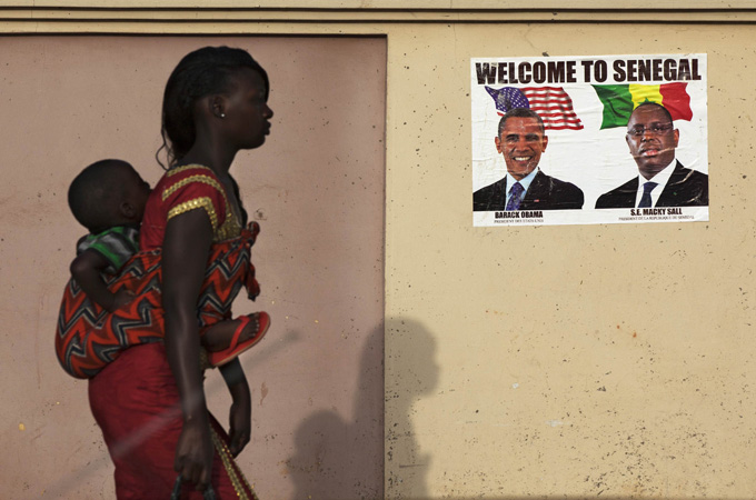 A woman carrying her baby on her back walks past a poster of U.S. President Obama and Senegal''s President Sall before Obama''s visit in Dakar