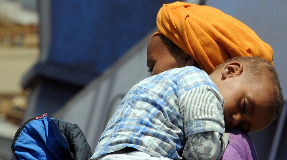 woman carries a baby as she disembarks from the German Navy ship Hessen at the Palermo