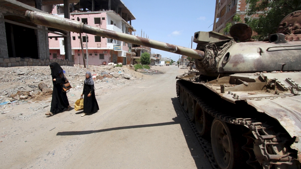 Woman and a girl walk past a broken-down tank on a street in Yemen''s southern port city of Aden
