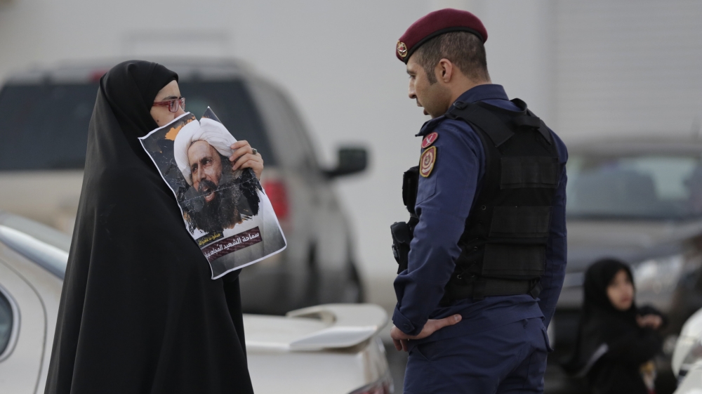A Bahraini protester holds up a picture of Saudi Shiite cleric Sheikh Nimr al-Nimr toward a riot police officer in Daih