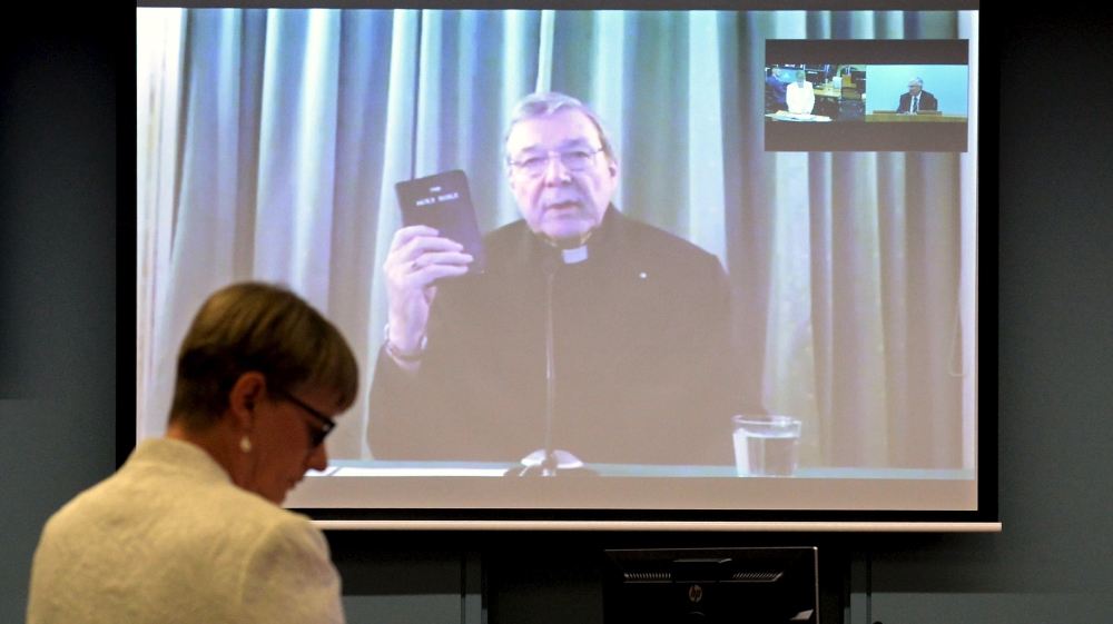 Senior Counsel Assisting Gail Furness stands in front of a screen displaying Australian Cardinal George Pell as he holds a bible while appearing via video link from a hotel in Rome, Italy t