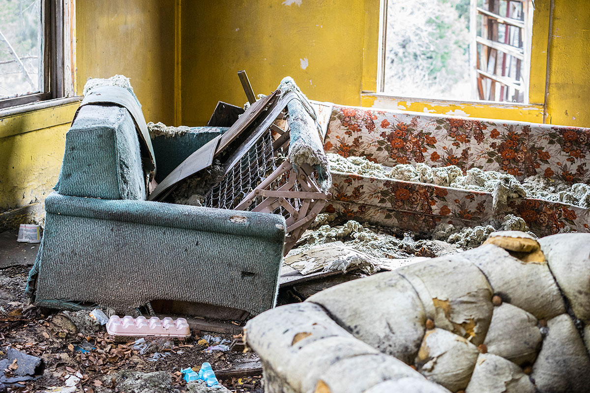 The intimate decay of a family living room in an abandoned house. The insides of the pull-out couch cover the broken floorboards [Gabriela Campos/Al Jazeera]