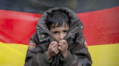 A child tries to warm his hands, in front of the Germany flag in Idomeni, Greece. [AP]