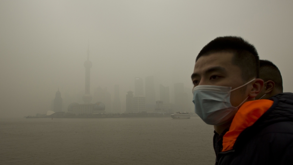 A man wears a face mask while walking on the Bund in front of the financial district of Pudong during a hazy day in downtown Shanghai