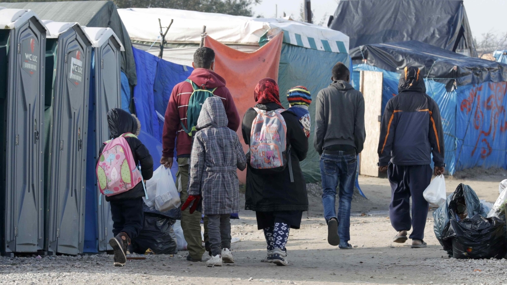 Migrants carry their belongings as they walk in an alley near tents and makeshift shelters on the eve of the evacuation and dismantlement of the camp called the "Jungle" in Calais