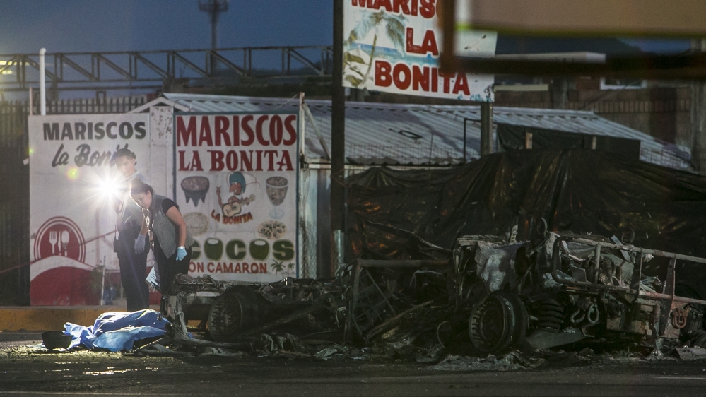 Police investigators stand over a body at the site where a military convoy was ambushed with grenades and high-powered guns