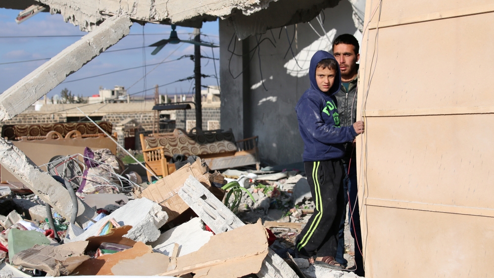 Civilians stand in a damaged house after an airstrike in the rebel-held southern town of Bosra al-Sham