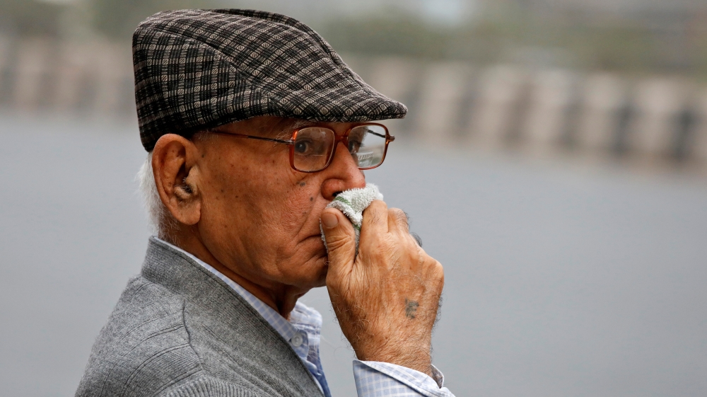 A man uses a piece of cloth to cover his nose as he waits for a passenger bus on a smoggy morning in New Delhi