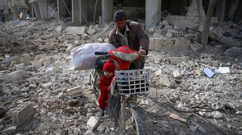 A man is seen with a child who rides a bicycle inside damaged area in Misraba, Eastern Ghouta, near Damascus