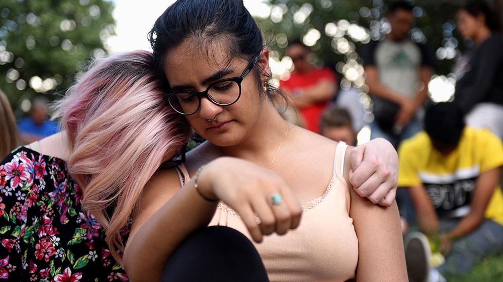 Two women embrace as people gather for a vigil following Saturday’s shooting in Odessa, Texas