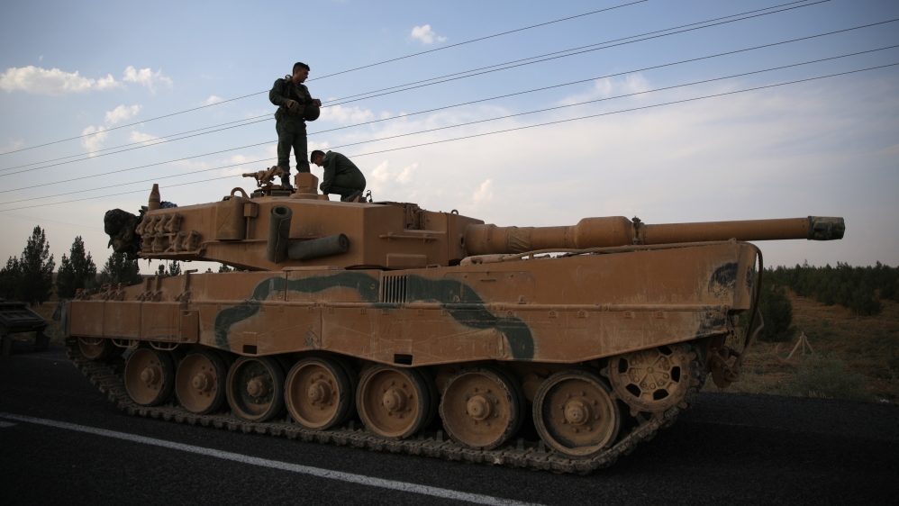 Turkish soldiers stand atop of a tank as army vehicles are moving on a road near the Turkish border town of Ceylanpinar