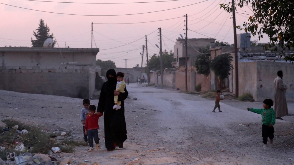 A woman holds a child as she walks along a street in the border town of Tal Abyad, Syria