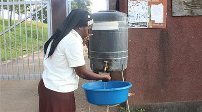 A visitor sanitizes her hands with chlorine water before entering Bwera Hospital near Mpondwe, Uganda