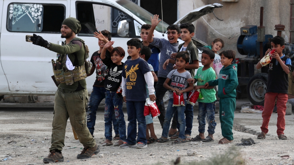 A Turkey-backed Syrian rebel fighter takes a picture with children on his mobile phone in the border town of Tal Abyad, Syria