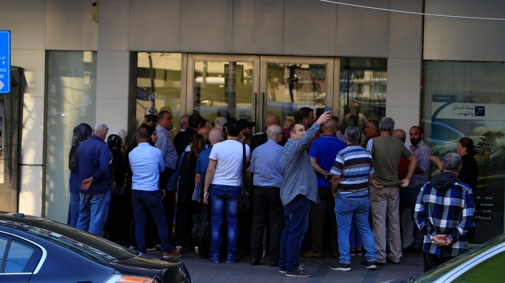 A man takes a picture with his mobile phone as people queue outside a branch of Blom Bank in Sidon