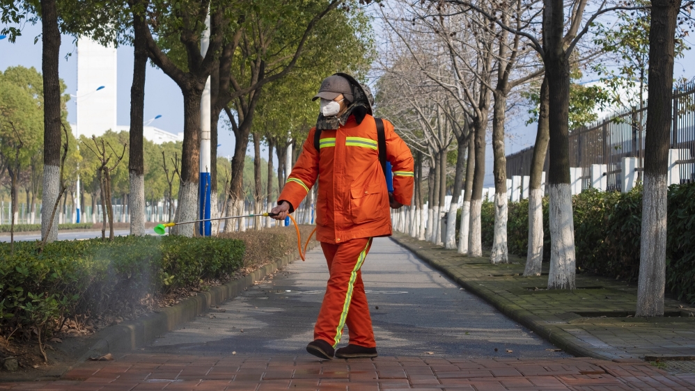 A worker wearing a face mask sprays disinfectant along a path in Wuhan which has been sealed off to try and curb the spread of the virus