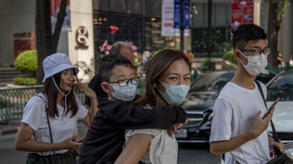 Chinese family wearing face masks walk in a pedestrian crossing in Bangkok, Thailand, Wednesday, Jan. 29, 2020. Tourism Council of Thailand said Tuesday that new coronavirus outbreak estimated to cost