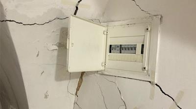 Cracks in the wall are seen by the circuit breaker in Hanan Slaima’s home