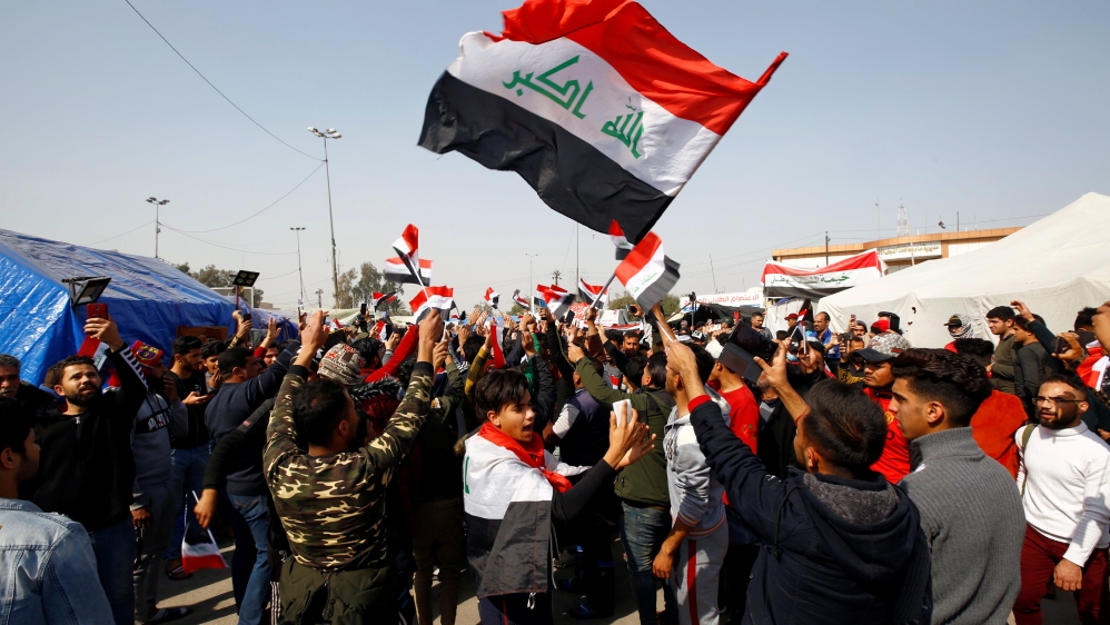 Iraqi demonstrators hold the Iraqi flag as they chant slogans during ongoing anti-government protests in Najaf