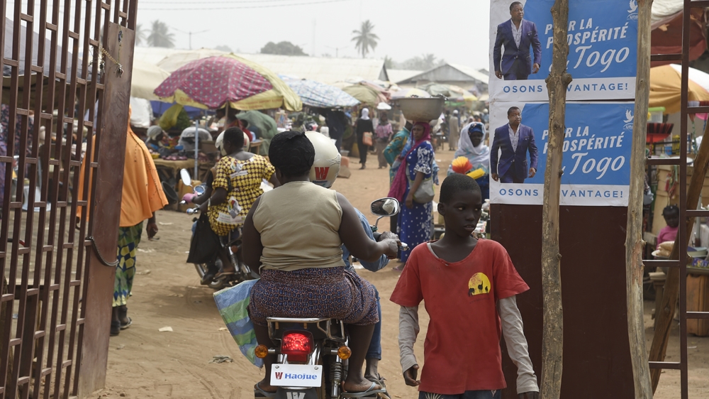 A motorbike taxi drive past campaign banners of Togolese President