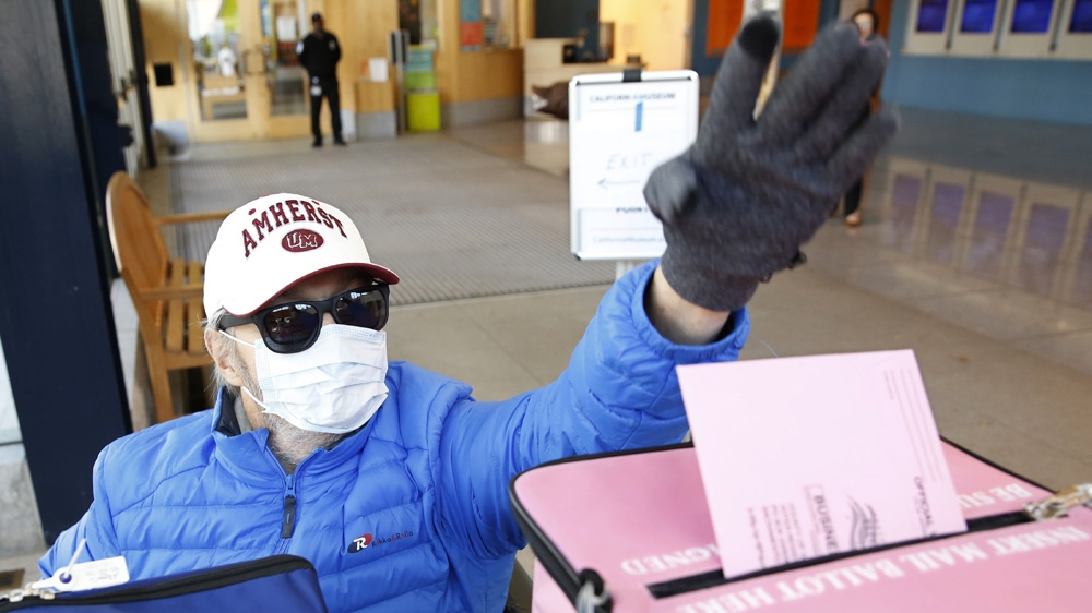 Wearing a mask as a precaution against passing or receiving germs, Joseph Dorocak casts his ballot on the eve of Super Tuesday at a voting center in Sacramento