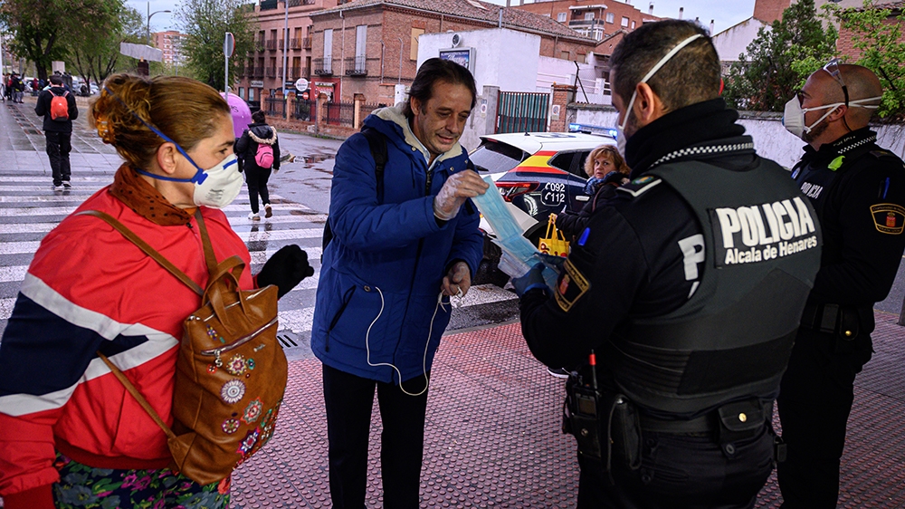 epa08359981 Policemen hand in masks to commuters at the train station in Alcala de Henares, Madrid, Spain, as many return back to work, 13 April 2020. Many people from various sectors return back to w