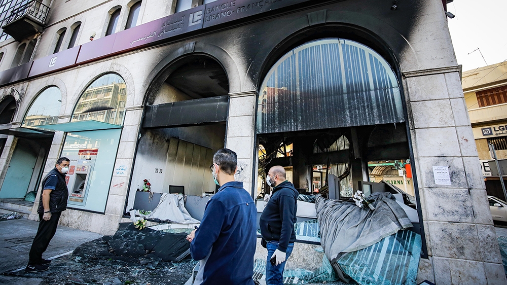 People inspect a bank set ablaze overnight by protesters
