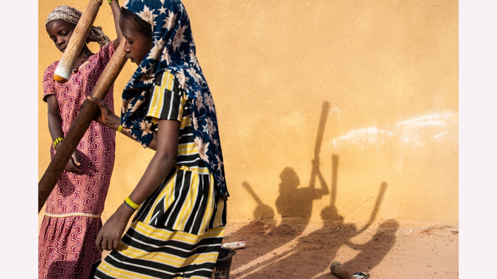 Young girls grind cornmeal on what was once was a school day in Mopti, Mali; their village was attacked and burned to the ground, so they now spend their days doing chores at a camp for displaced people