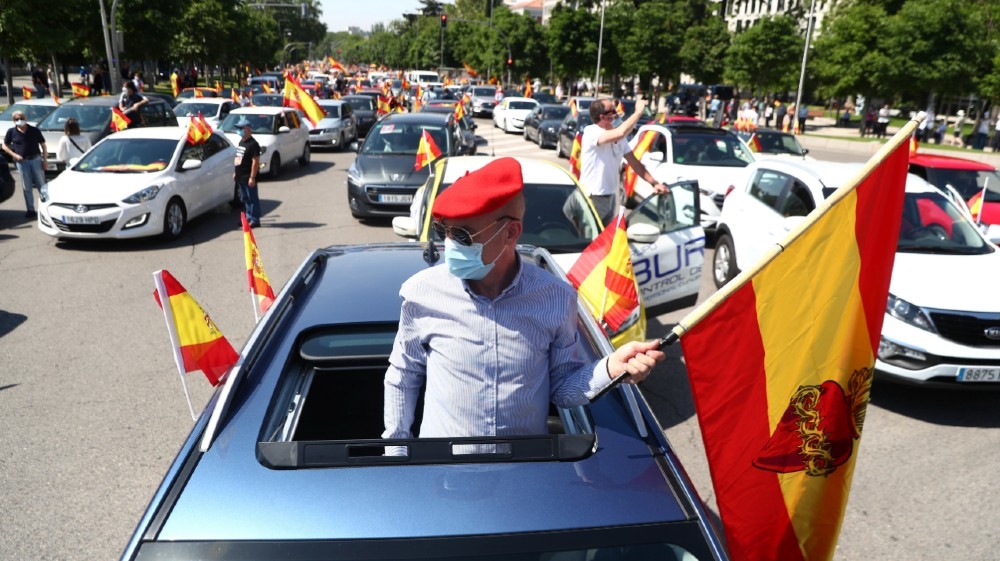 A demonstrator wearing a protective face mask carries a flag during a drive-in protest organised by Spain's far-right party Vox against the government's handling of the