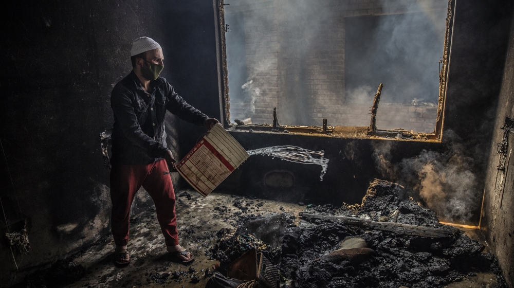 A Kashmiri man douses a fire in a house which was damaged in a gun-battle in Srinagar, Indian controlled Kashmir, Tuesday, May 19, 2020. Indian government forces killed two rebels in disputed Kashmir