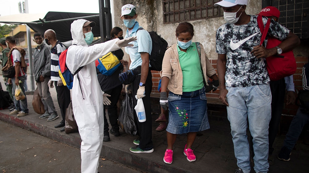A city worker, dressed in protective gear, asks people waiting for a bus to maintain a safe social distance as a measure to curb the spread of the new coronavirus in Caracas, Venezuela