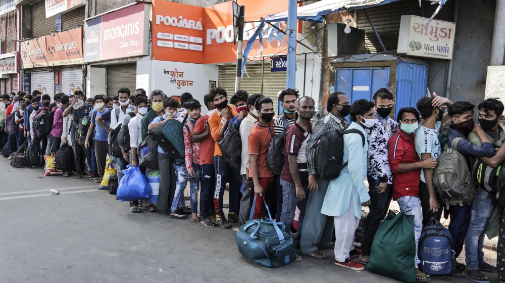 Migrant workers from other states trying to return to their homes stand in queue as they wait for transportation to a train station in Ahmedabad, India, Sunday, May 17, 2020. Tens of thousands of migr