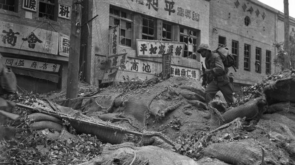 A US marine clambers over a battered and shell-splattered barricade in a Seoul business district at the height of fighting for the South Korean capital held by invading North Koreans for three months, September 28, 1950