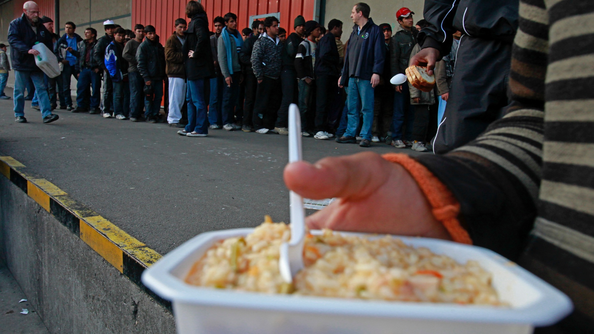 Asylum seekers queue outside a charity awaiting food distribution