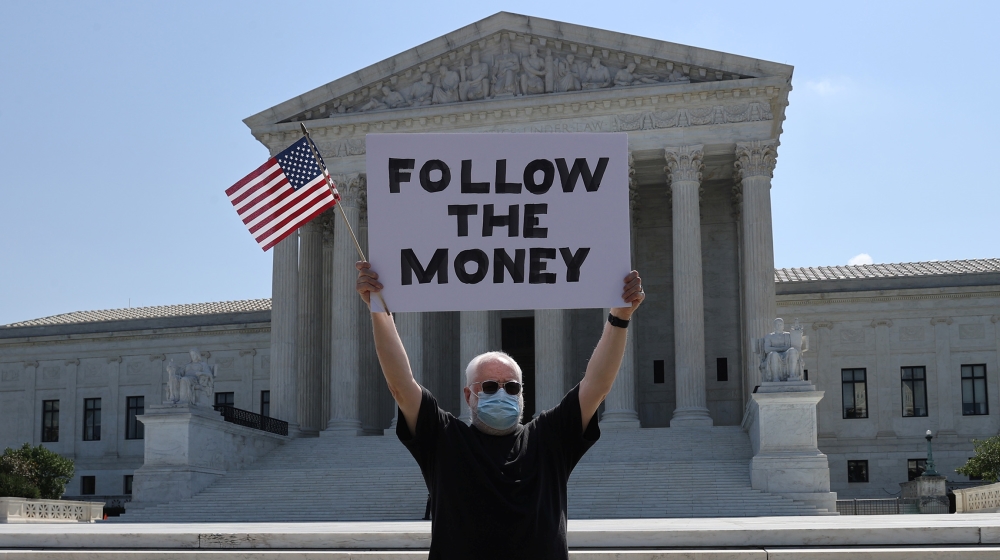 Bill Christeson holds a sign reading "follow the money" in anticipation of a U.S. Supreme Court ruling on U.S. President Donald Trump''s bid to block his financial records from being obtained by third