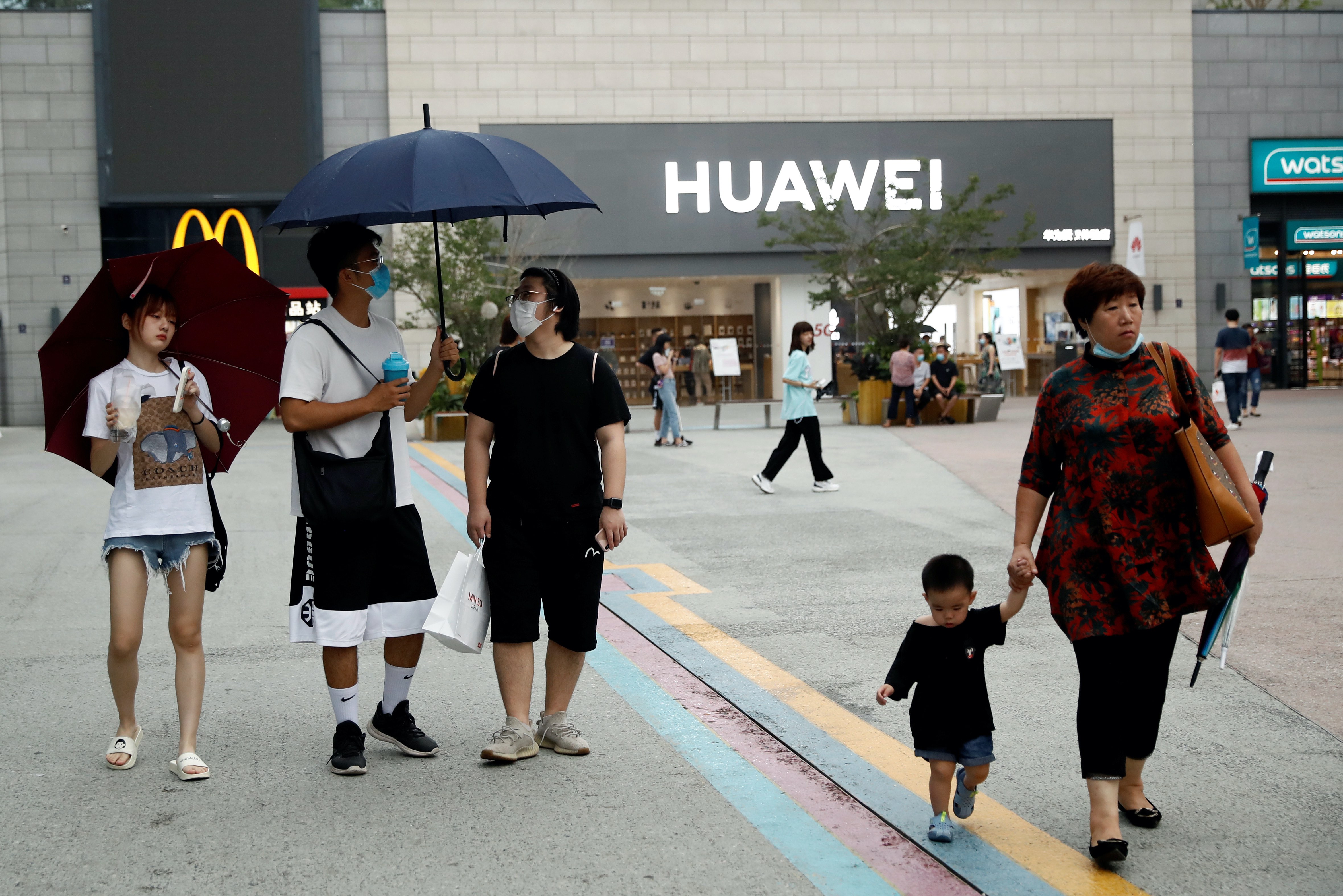 People wear protective face masks as they walk near a Huawei store in a shopping complex in Beijing