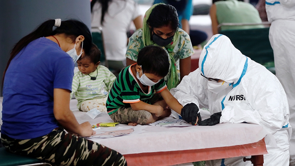 A medical worker helps a boy draw inside a care centre for coronavirus patients at an indoor sports complex in New Delhi
