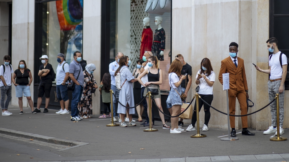 People with face masks queue as they wait to get in the Louis Vuitton shop on the Champs Elysee avenue in Paris, Saturday, Aug. 15, 2020. Paris extended the areas of the city where pedestrians will be