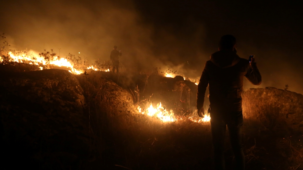 A man uses his phone near a fire in Houla village near the Lebanese-Israeli border, in southern Lebanon