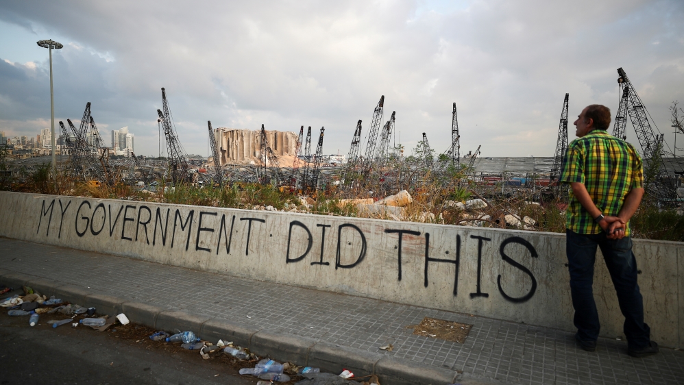 A man stands next to graffiti at the damaged port area in the aftermath of a massive explosion in Beirut