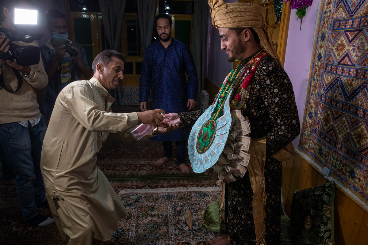 A Kashmiri man sprays sanitizer on the hand of Haseeb Mushtaq, a Kashmiri groom as he arrives at brides home during his wedding ceremony on the outskirts of Srinagar, Indian controlled Kashmir, Monday