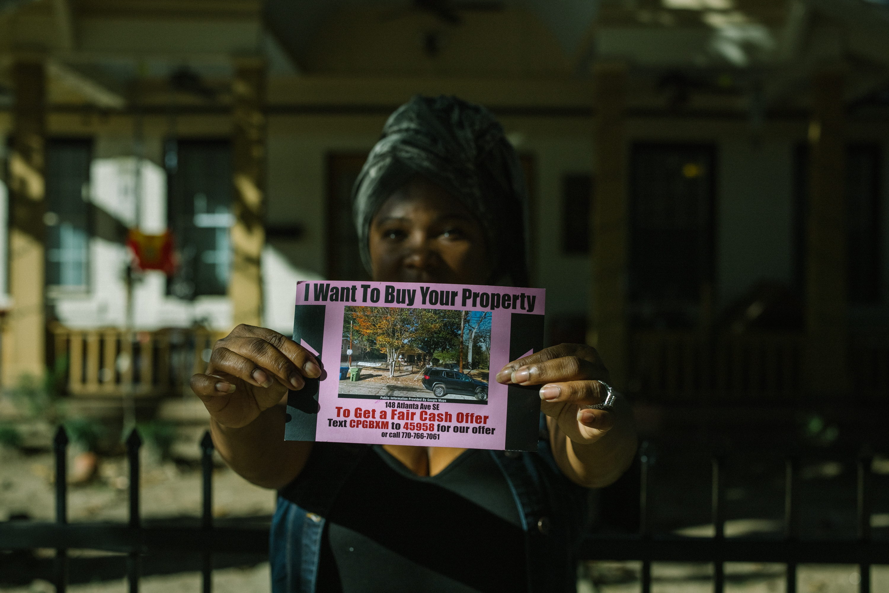 Tanya Washington holds a photo of one of the real estate postcards that private realtors send to residents in Peoplestown. It has a picture of her house on it, urging her to sell