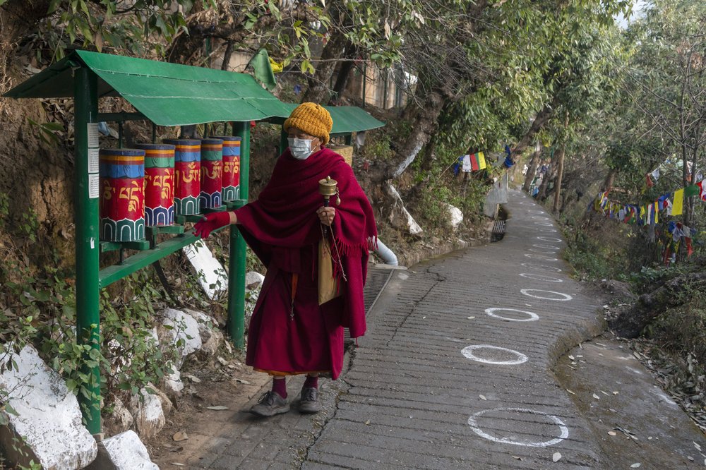 An in exile Tibetan Buddhist monk rotates prayer wheels next to a path marked with circles for voters to ensure social distancing [AP Photo]