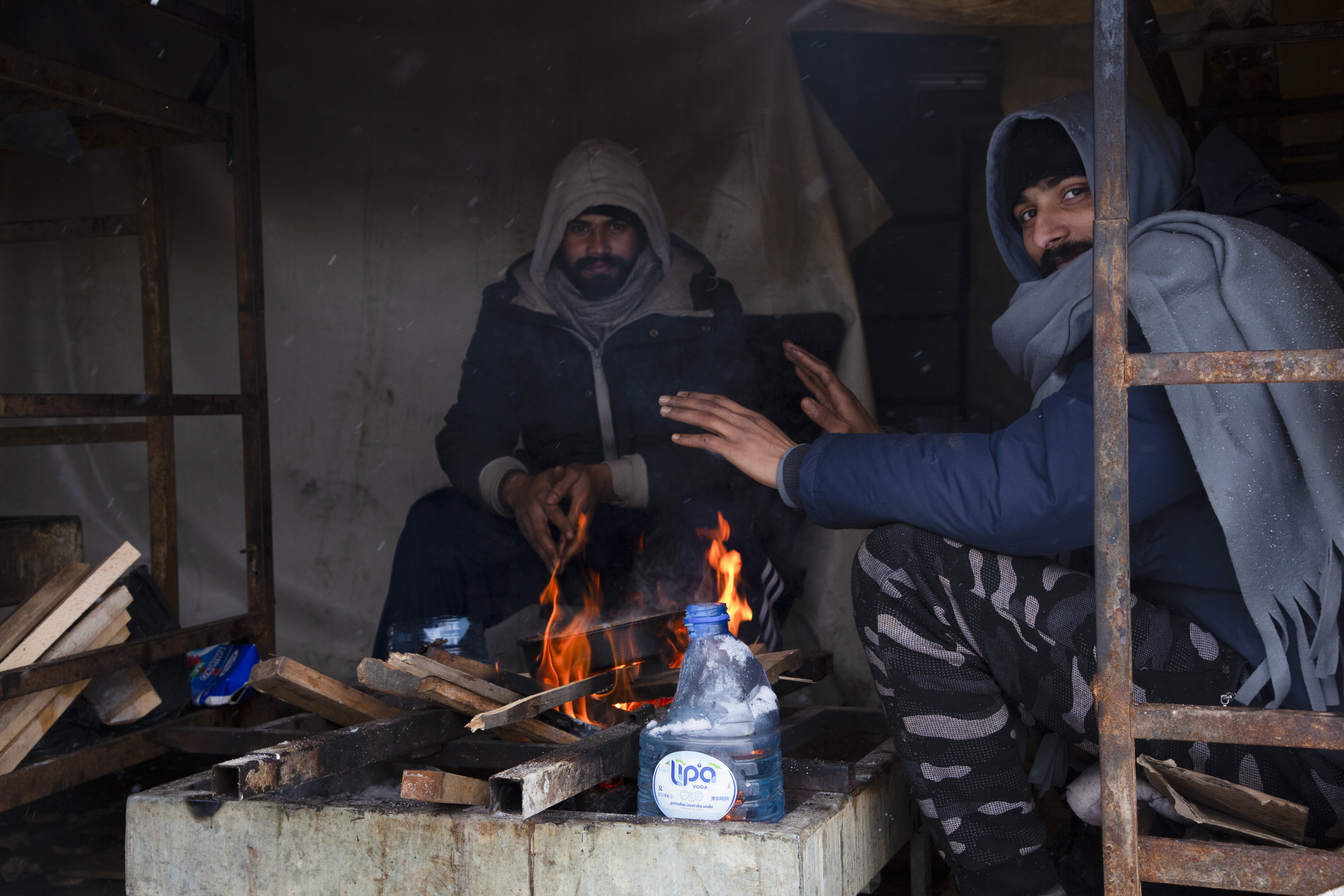 A 22-year-old man from Pakistan (right) sits with a friend around a fire in a makeshift shelter on the site of the former Lipa camp