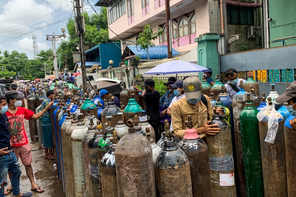 People stand with empty oxygen canisters as they wait to fill them up outside a factory in Yangon on Sunday, amid a surge in COVID-19 coronavirus cases