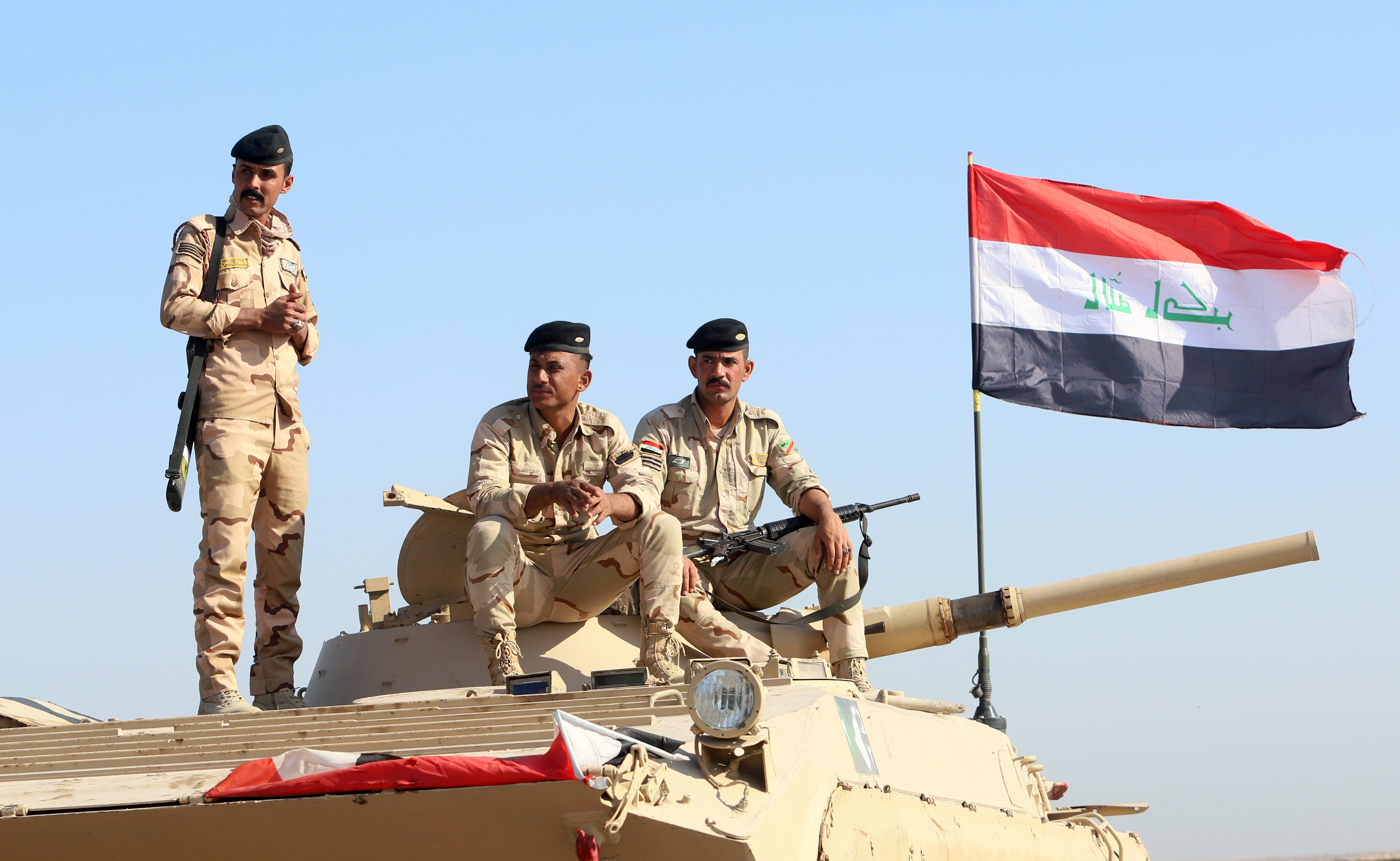 Iraqi army officers sit on a military vehicle.