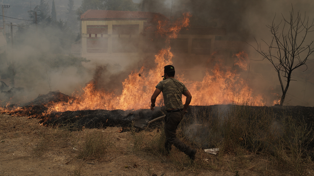 A resident of Ippokratios Politia, near Athens, tries to extinguish a fire [Nick Paleologos/Al Jazeera]
