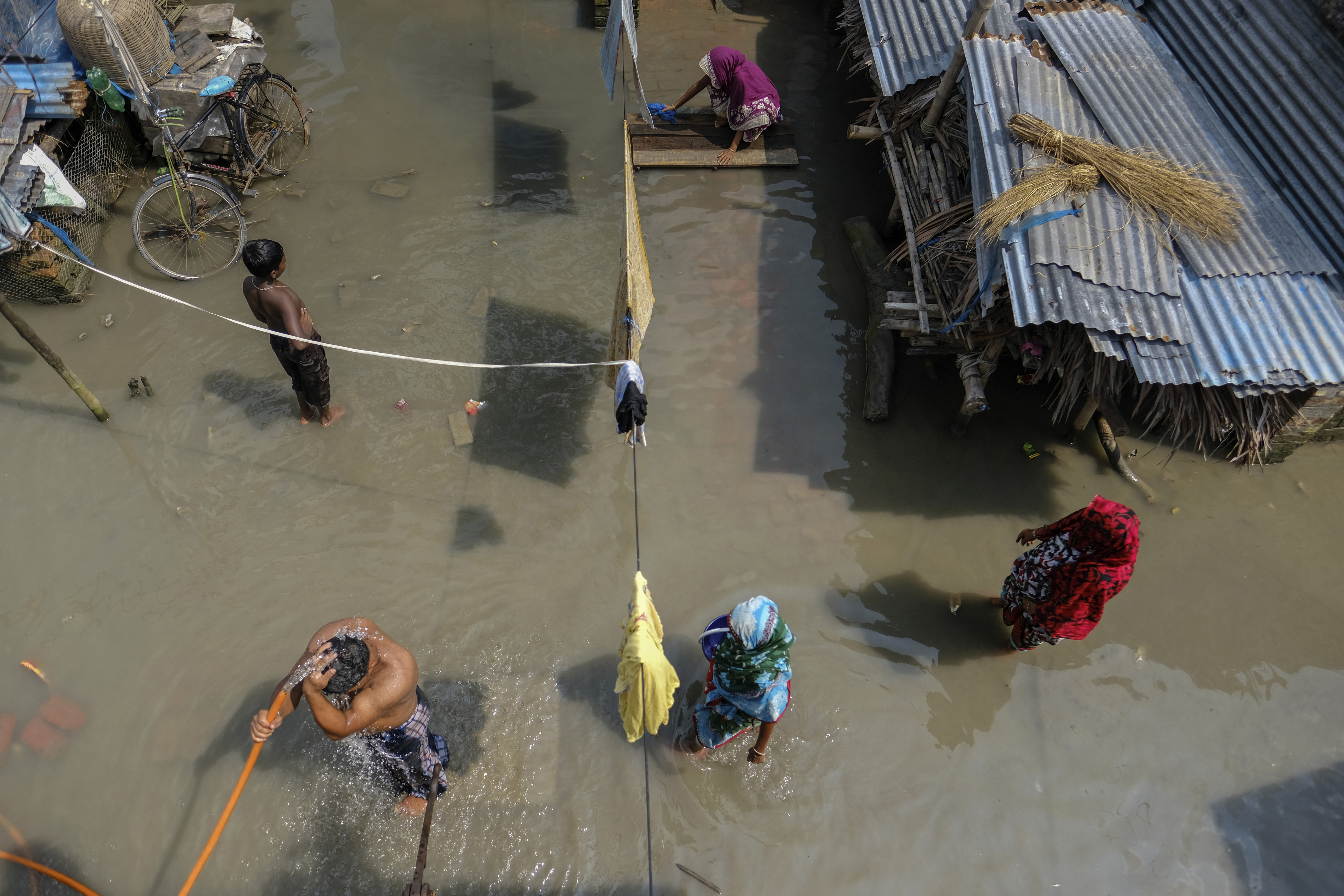 A man bathes as a woman performs chores outside her inundated house in Pratap Nagar, in Shyamnagar area, Satkhira, Bangladesh