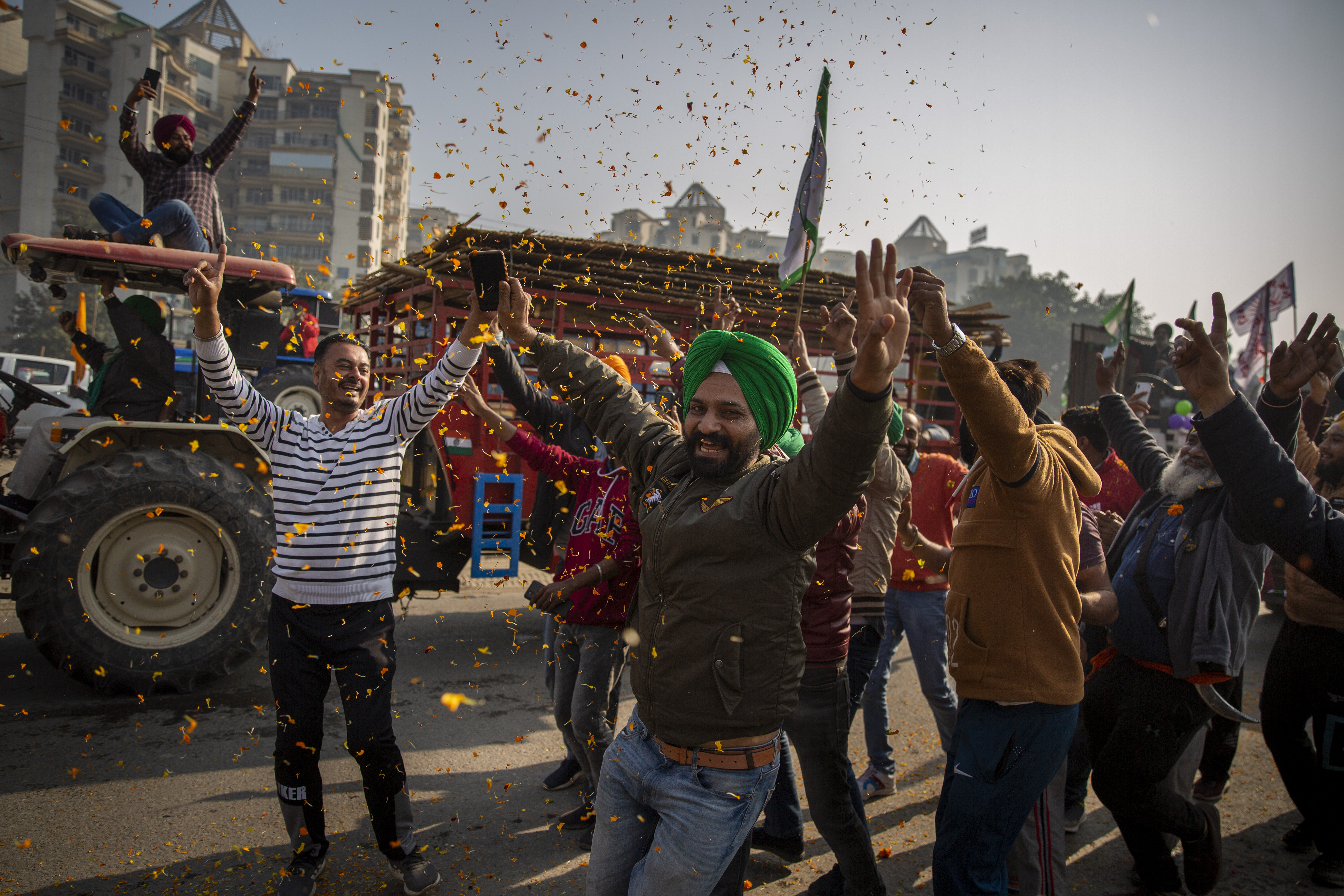 Indian farmers are showered with flower petals as they dance while leaving the protest site in Singhu, on the outskirts of New Delhi
