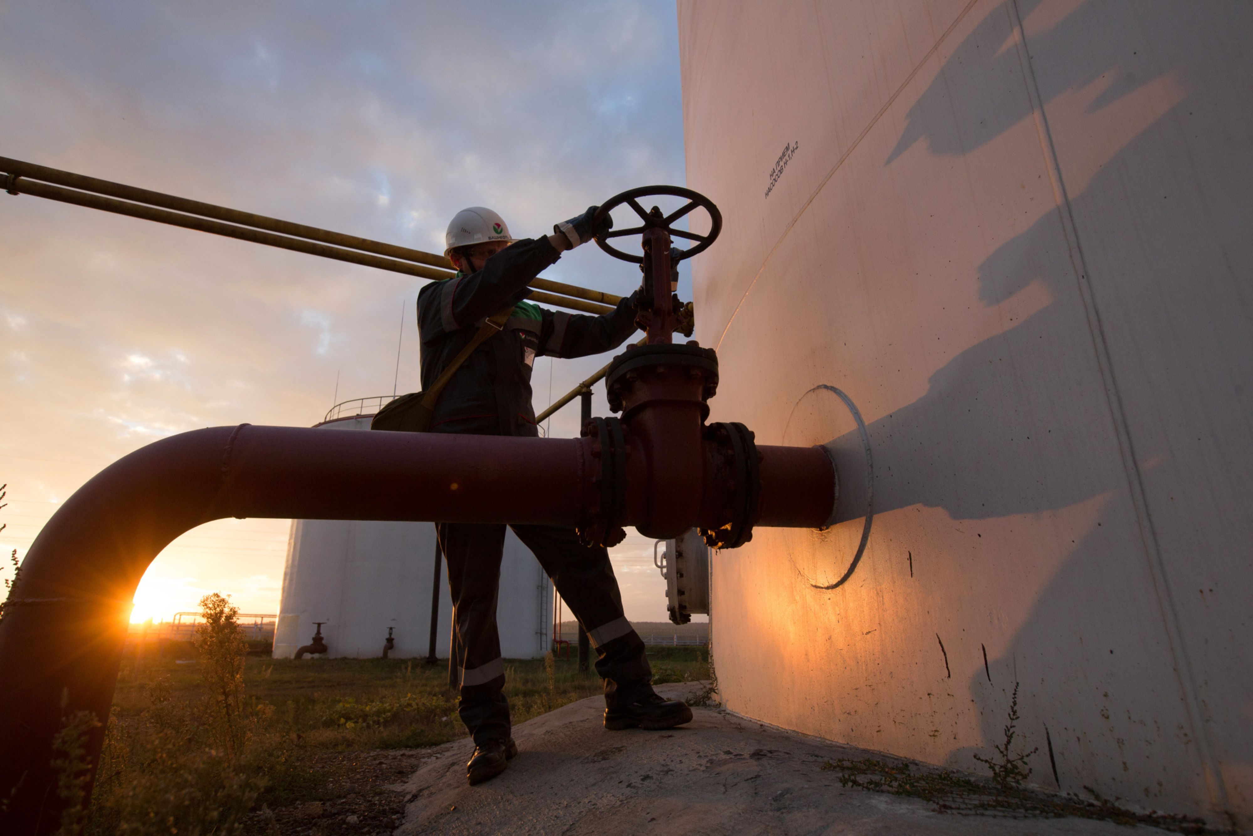 An employee turns a control valve on pipework beside a storage tank at an oil delivery point operated by Bashneft PAO in Sergeevka village, near Ufa, Russia